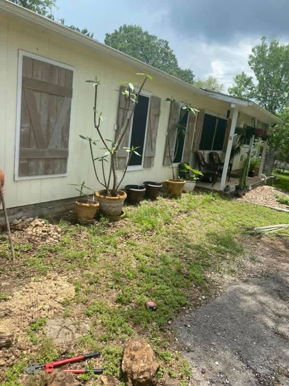 House exterior with boarded windows, potted plants, and a gravel path on a green lawn.