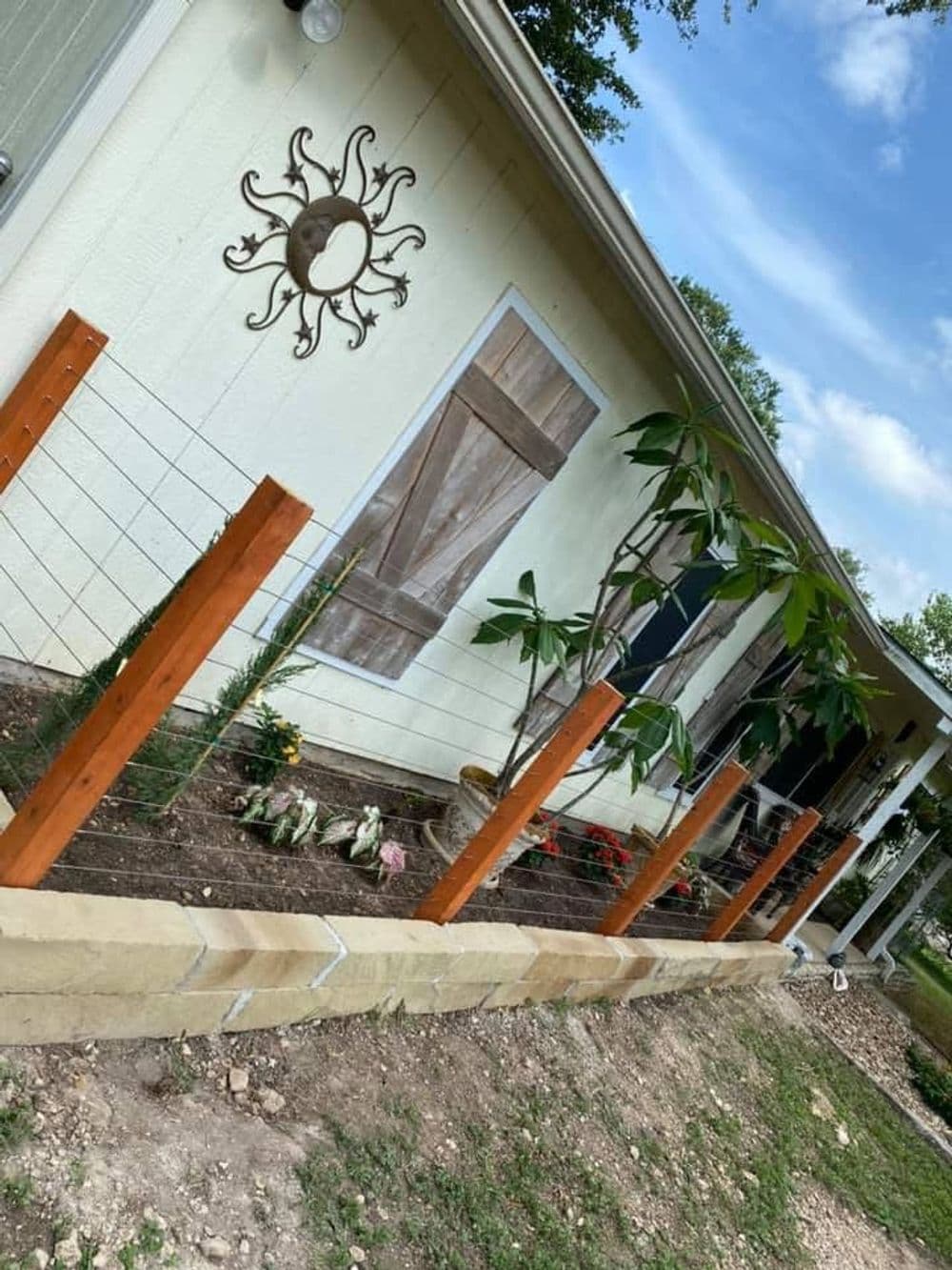 Front yard garden with wooden fence, sun decor, and flowering plants against a home backdrop.