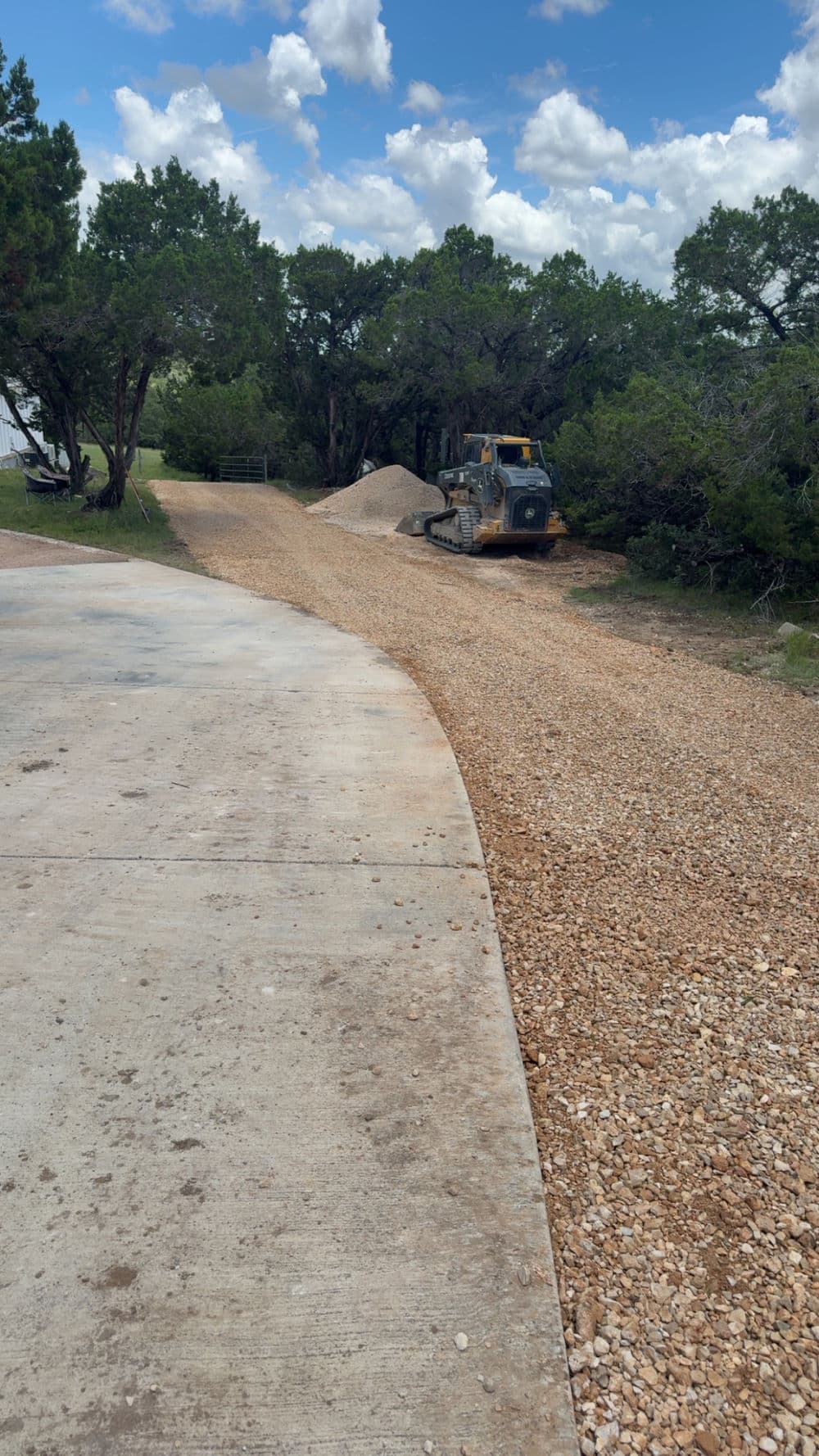 Gravel driveway under construction with a bulldozer and trees in the background.