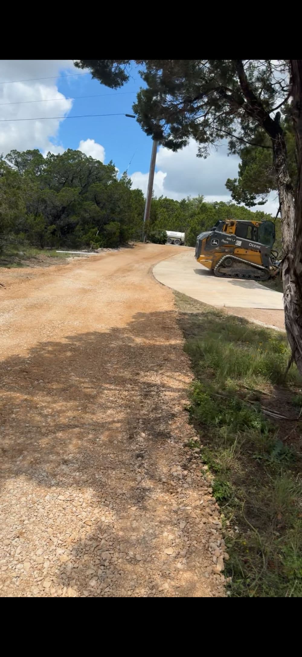 Gravel road winding through wooded area with construction vehicles, Texas landscape scene.