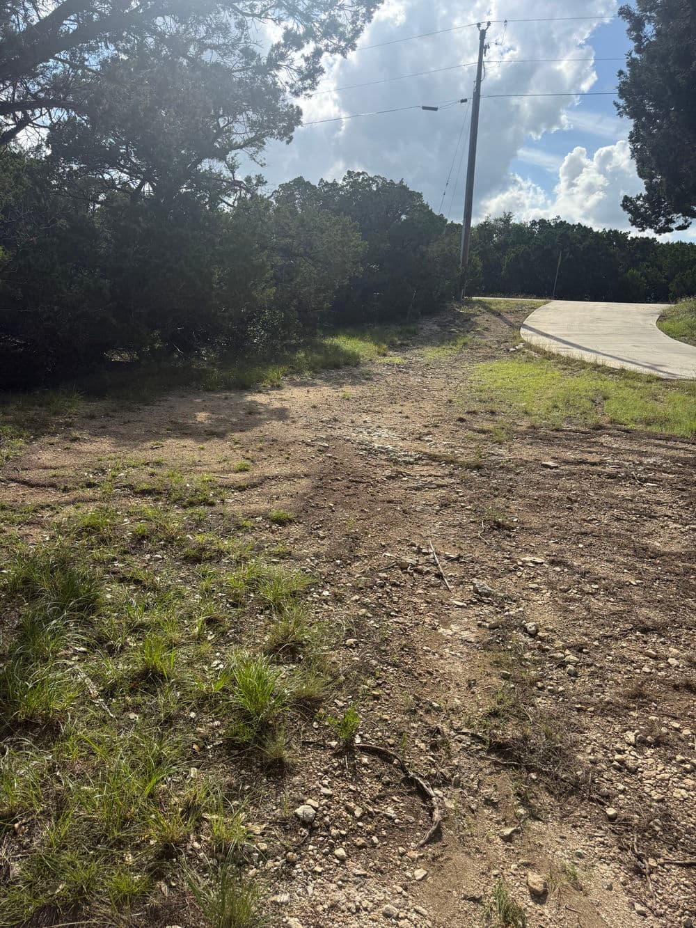 Dirt path leading through greenery near a road under a partly cloudy sky.