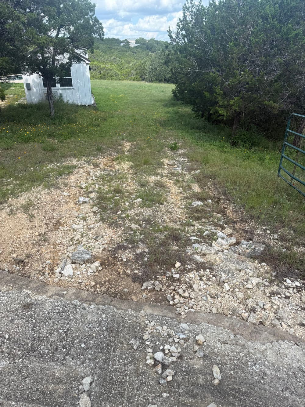 Gravel path leading to a grassy area with trees and a white building in the background.
