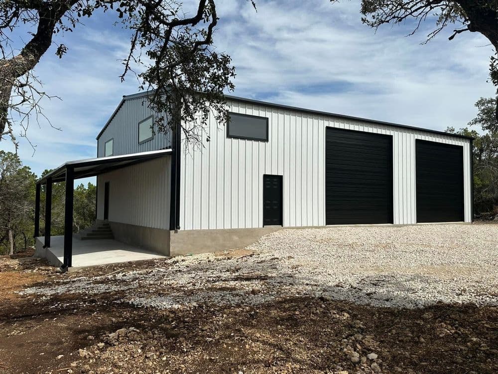 Modern metal building with large garage doors and covered porch in a rural setting.