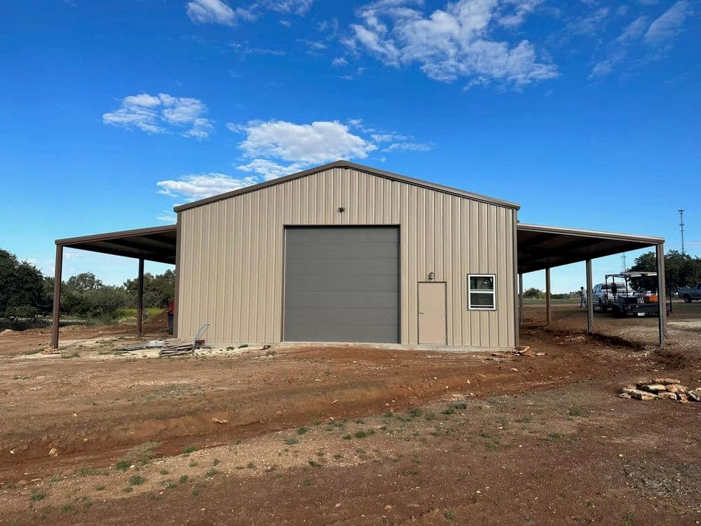Metal storage building with a large gray door, surrounded by open land and blue sky.