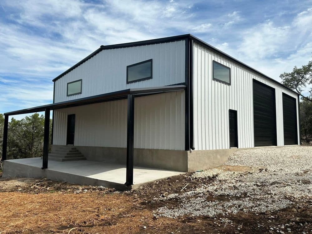 Modern metal building with a covered porch and large industrial doors, set in a rural landscape.