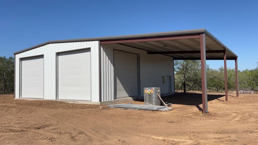 New metal storage building with roll-up doors in a rural setting under clear blue sky.