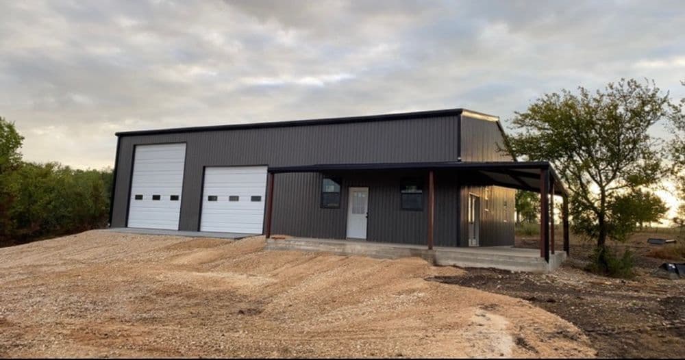 Modern metal building exterior with two large garage doors and gravel driveway.