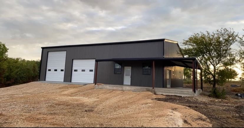 Newly built metal building with dual garage doors and porch in a rural setting.