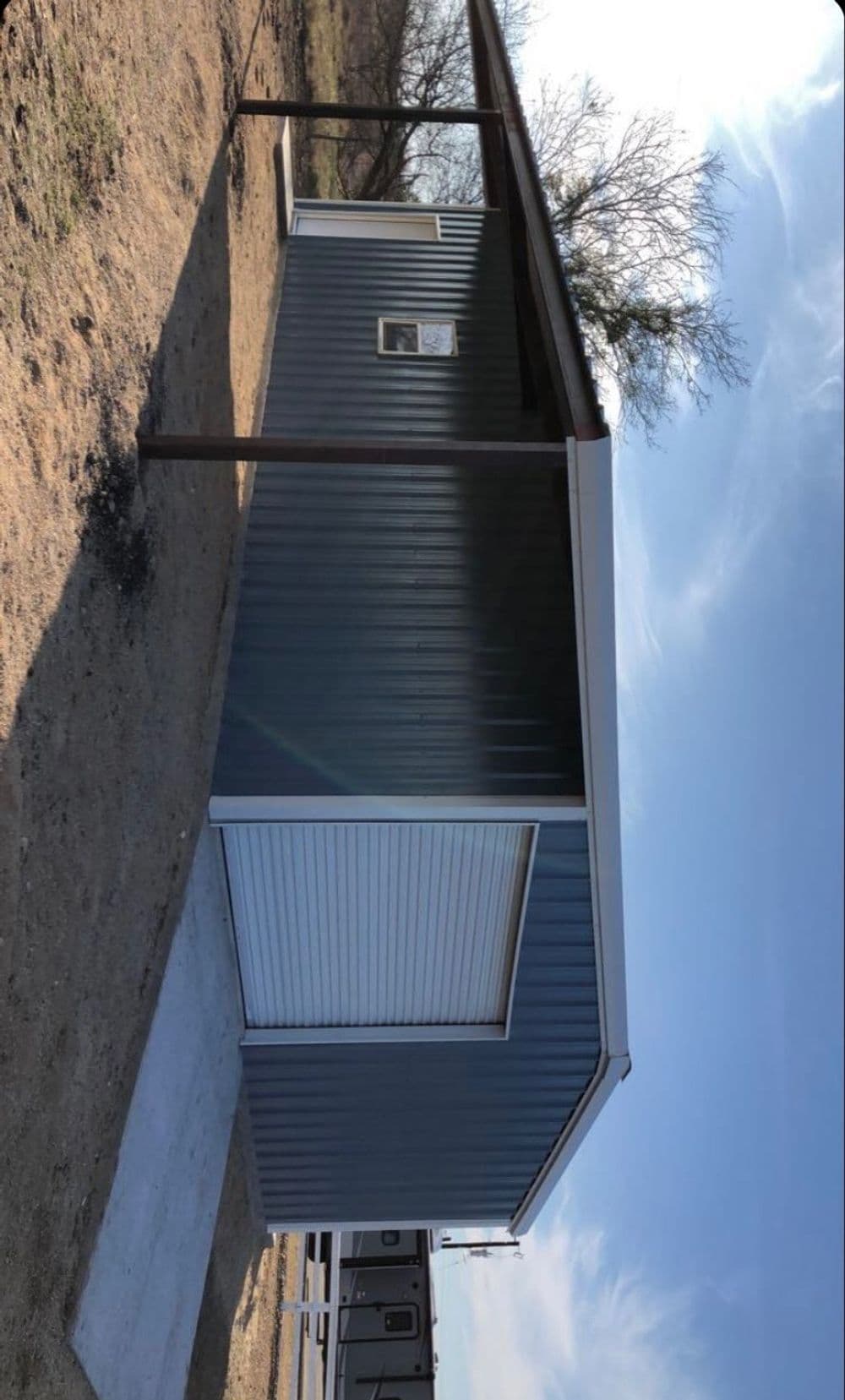 Metal storage building with a sloped roof, set on a concrete pad in a rural landscape.