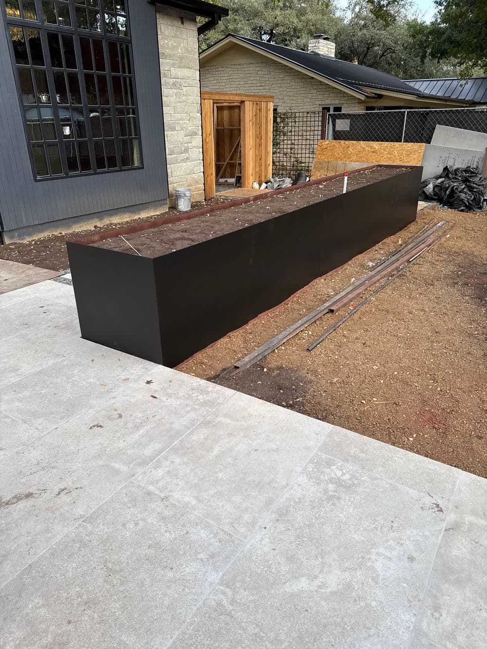 Modern black rectangular planter box in a construction landscape with gravel and tools.