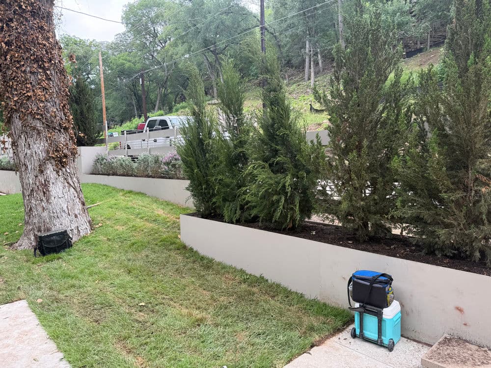Landscape featuring neatly trimmed shrubs, a cooler, and a gravel path in a peaceful garden setting.