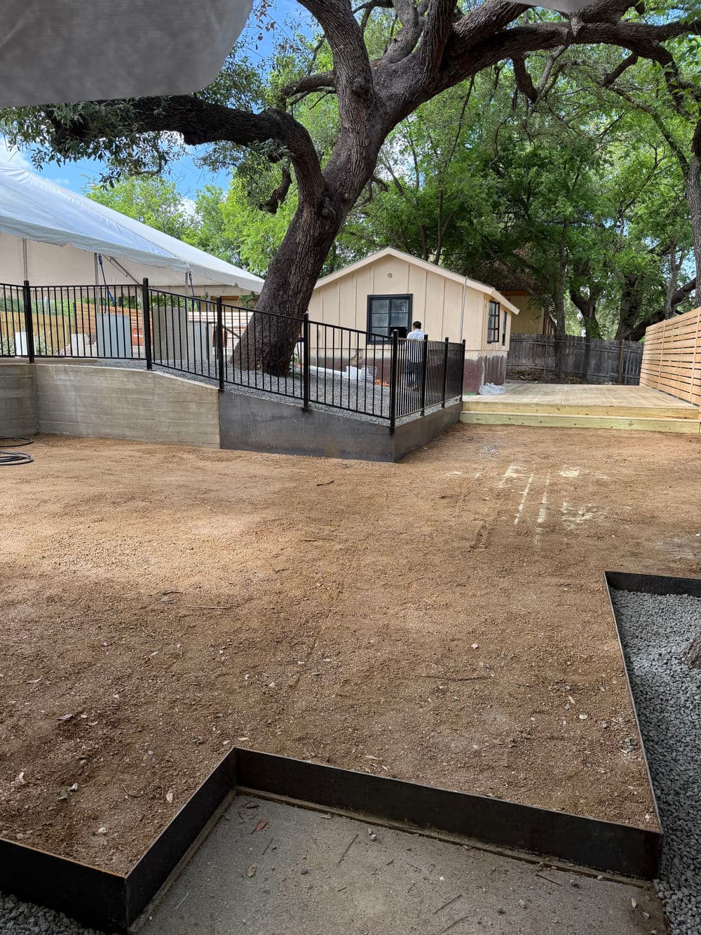 Renovated backyard with bare ground, fencing, and a house surrounded by trees.