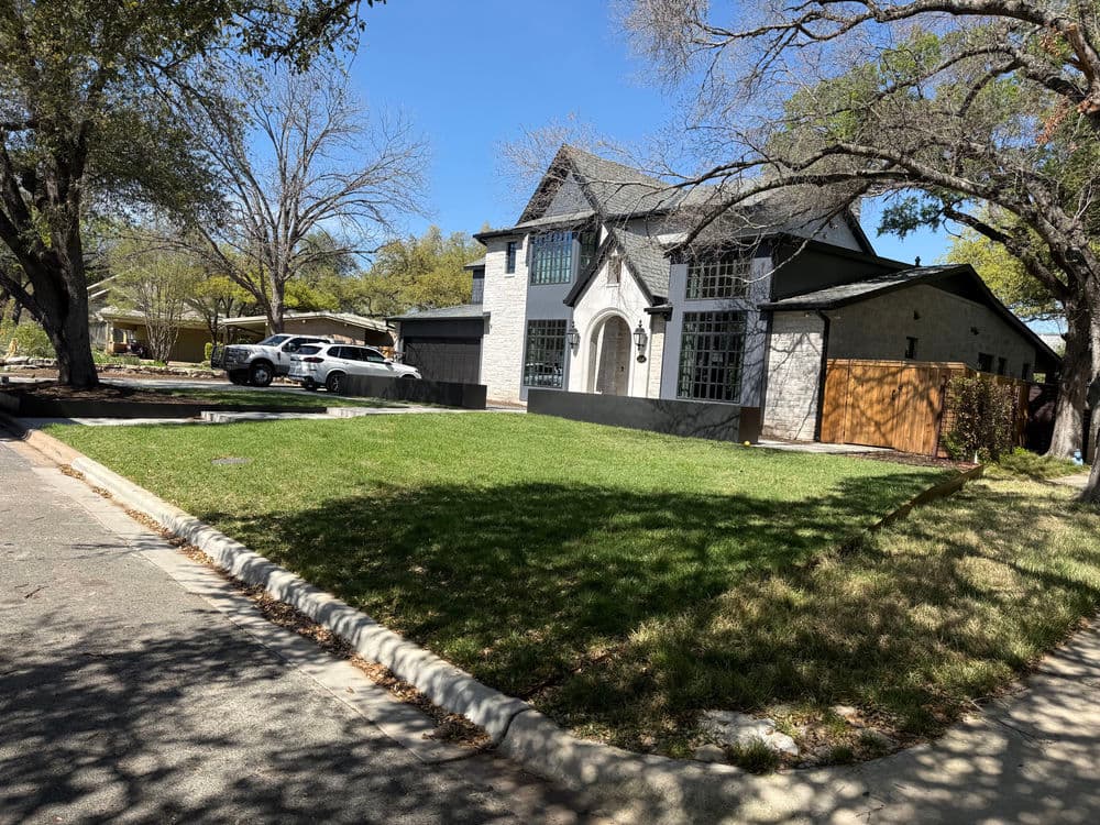 Modern two-story house with landscaped front yard and driveway on a sunny street.
