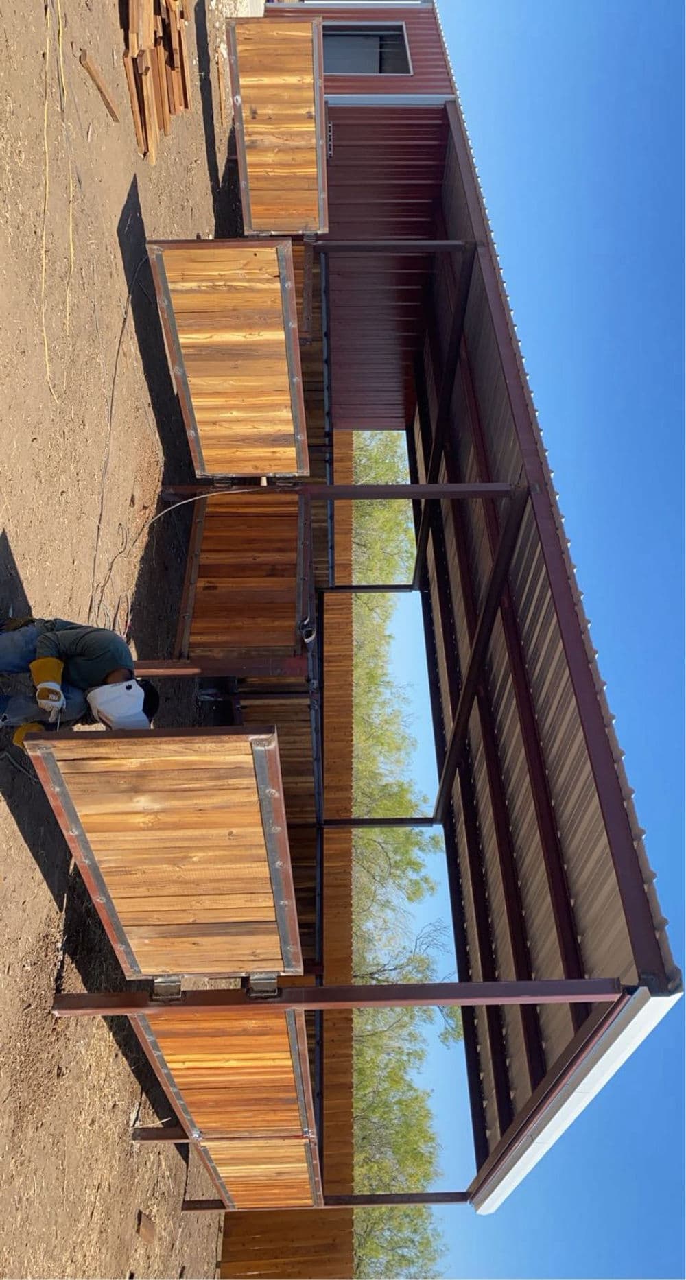 Wooden outdoor structure with a metal roof, featuring multiple stalls and open space.