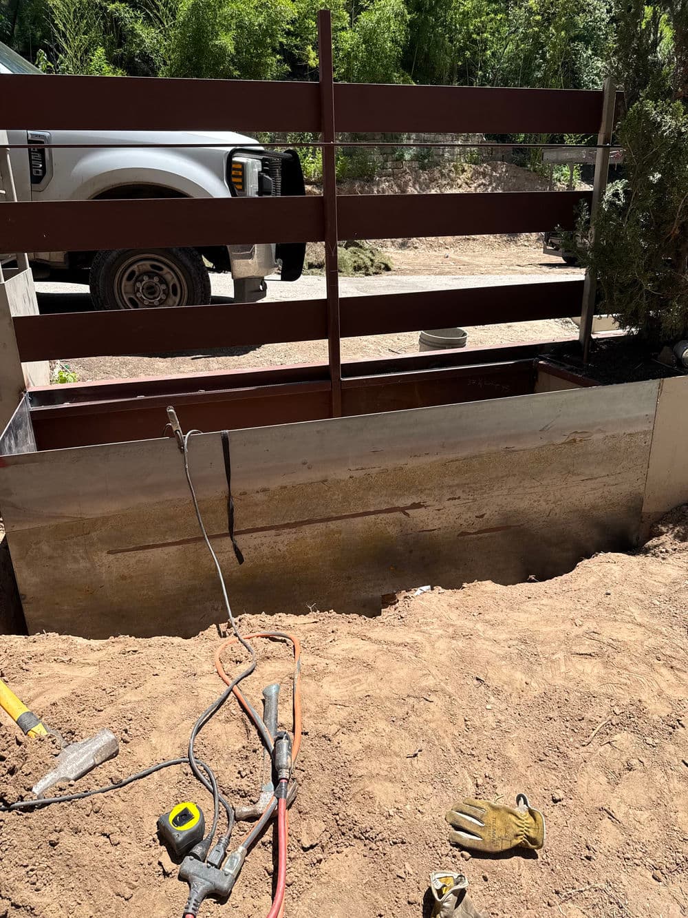 Excavation site with construction tools and a metal fence surrounding a concrete foundation.