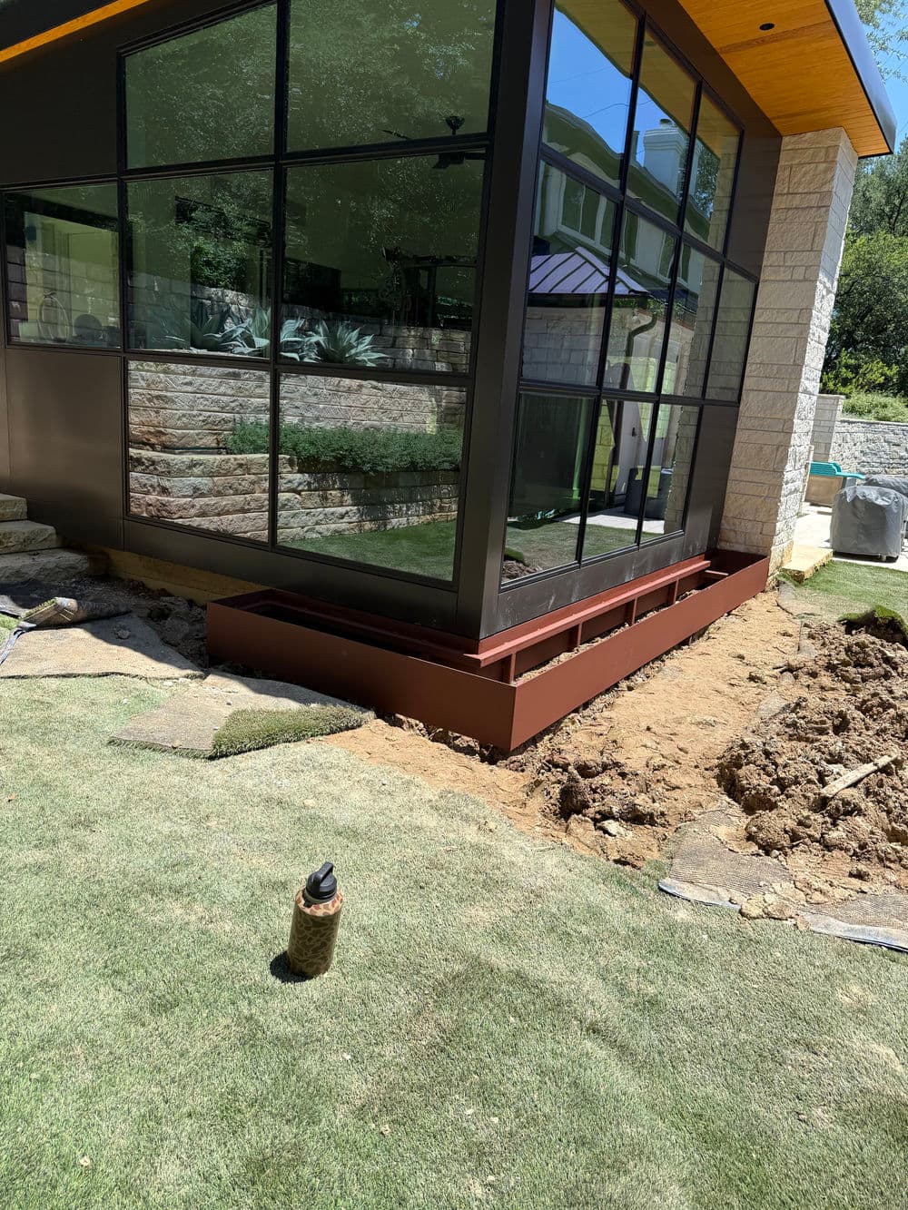 Modern home exterior with large windows and landscaped garden area under construction.