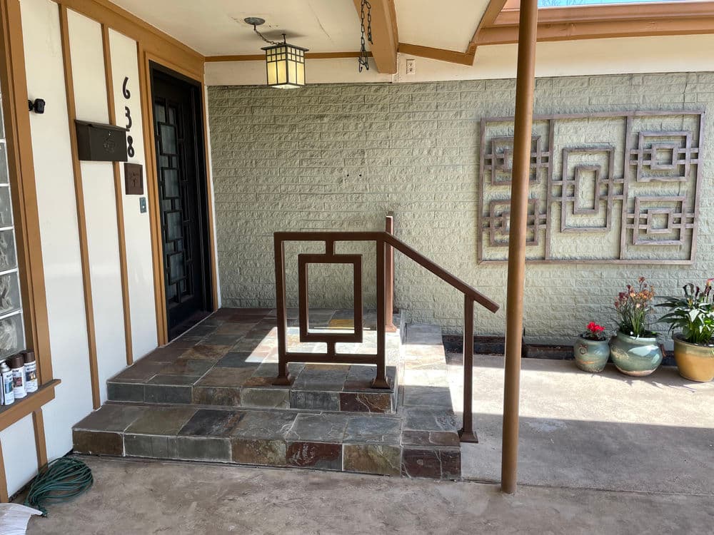 Front entrance with slate steps, decorative wall art, and landscaped planters.